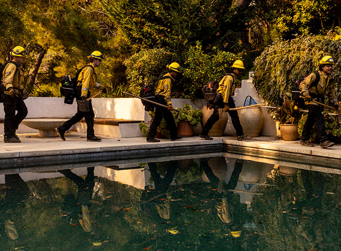 Private firefighters in yellow gear protect residential homes from wildfires, reflecting on a poolside path.