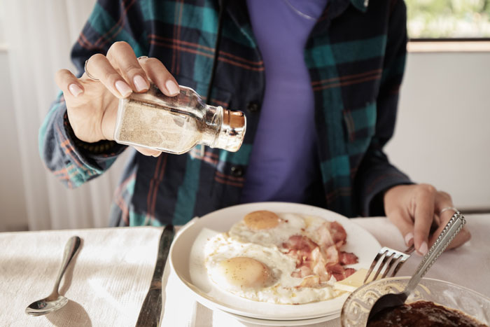 Person seasoning eggs at dinner party, with plaid shirt visible in frame, illustrating food waste theme.