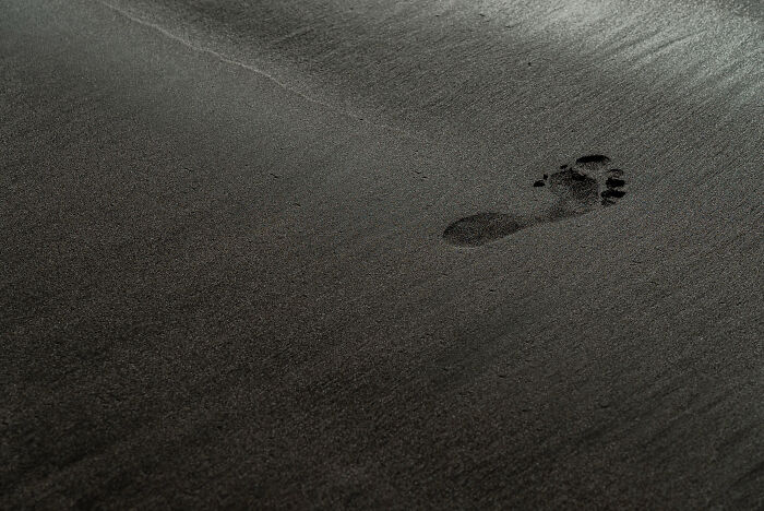 A single footprint in dark sand.