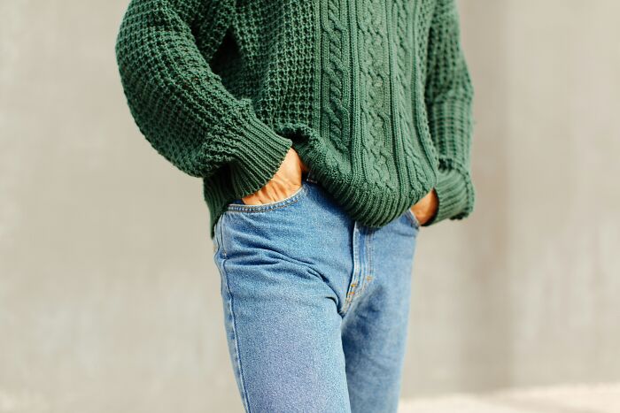 Person in a green knit sweater and blue jeans, hands in pockets.