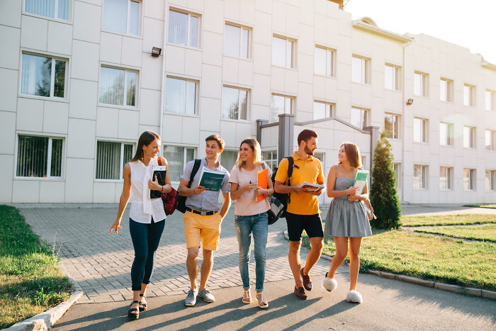 Young adults with books and backpacks walking, symbolizing unaffordable education for the middle class.