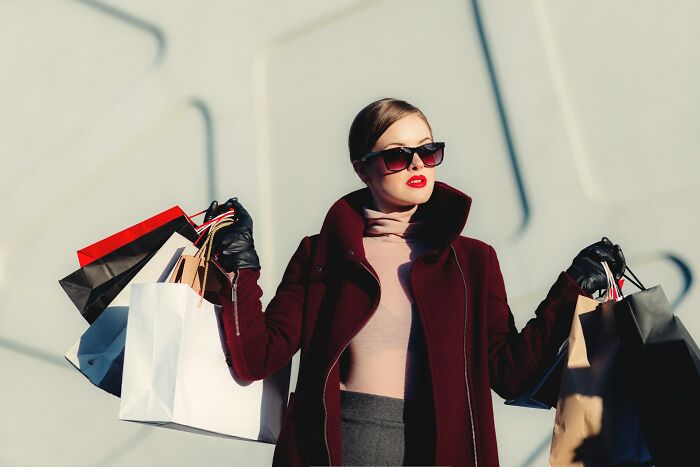 Person wearing sunglasses holding multiple shopping bags, challenging consumerism norms.