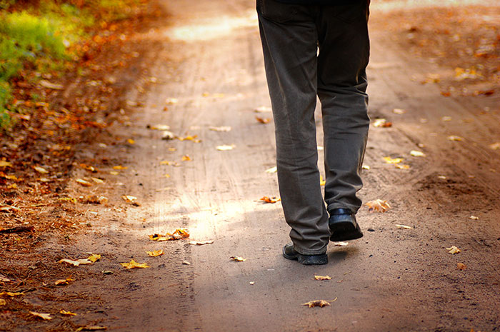 Person walking away on a leaf-strewn path, symbolizing being kicked out.