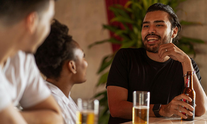 Friends chatting at a table, one holding a beer, discussing a home-cooked meal.