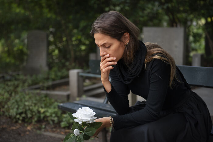 Woman in a cemetery holding a white rose, mourning a dead partner.