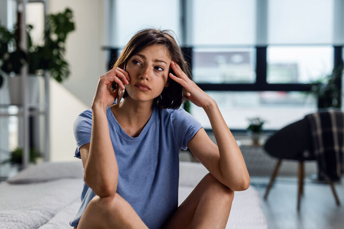 Woman on bed with thoughtful expression, arm to head, relating to friend and partner topics.