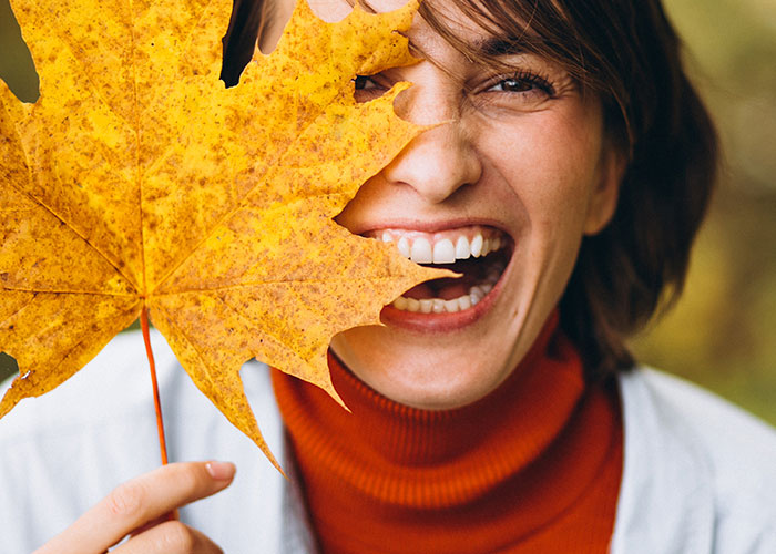 Woman laughing and holding a yellow maple leaf, wearing an orange turtleneck.