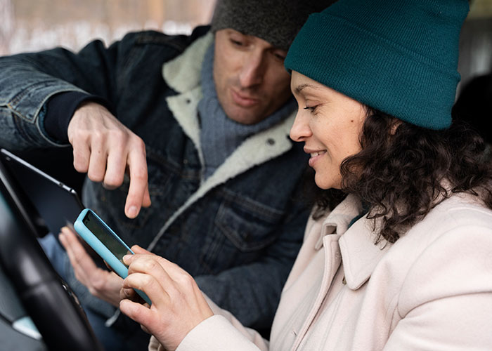 Man pointing at phone while woman in a teal hat listens, capturing a moment of mansplaining.