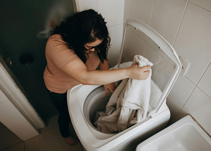 Woman placing laundry in washing machine, illustrating everyday tasks amidst gender discussions.