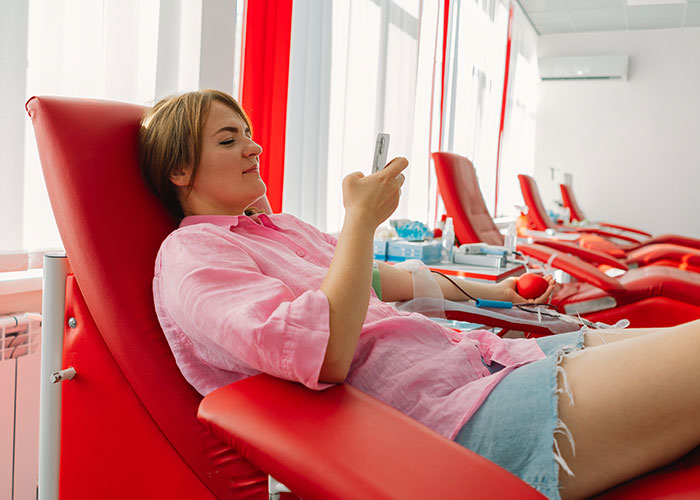 Woman relaxed in a donation chair, checking her phone, symbolizes moments guys might mansplain various topics.