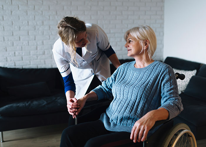 Healthcare worker assisting elderly woman in a wheelchair at home.