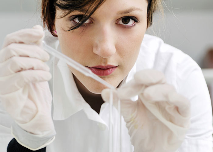 Woman in a lab coat, holding a pipette, focused on her work.