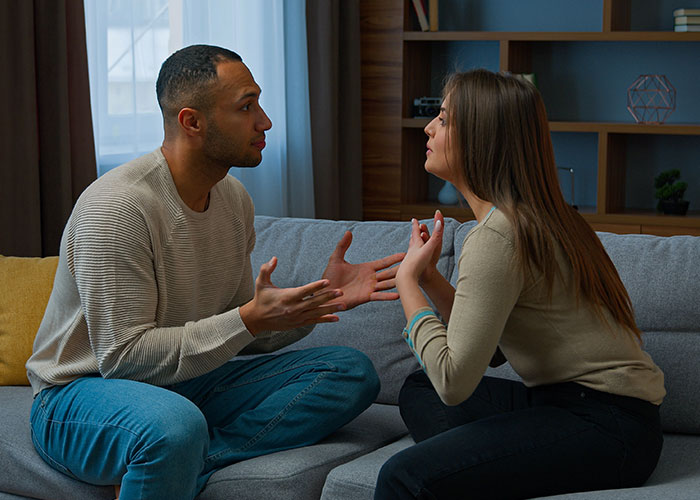 A man explaining something to a woman on a couch, while she listens skeptically.