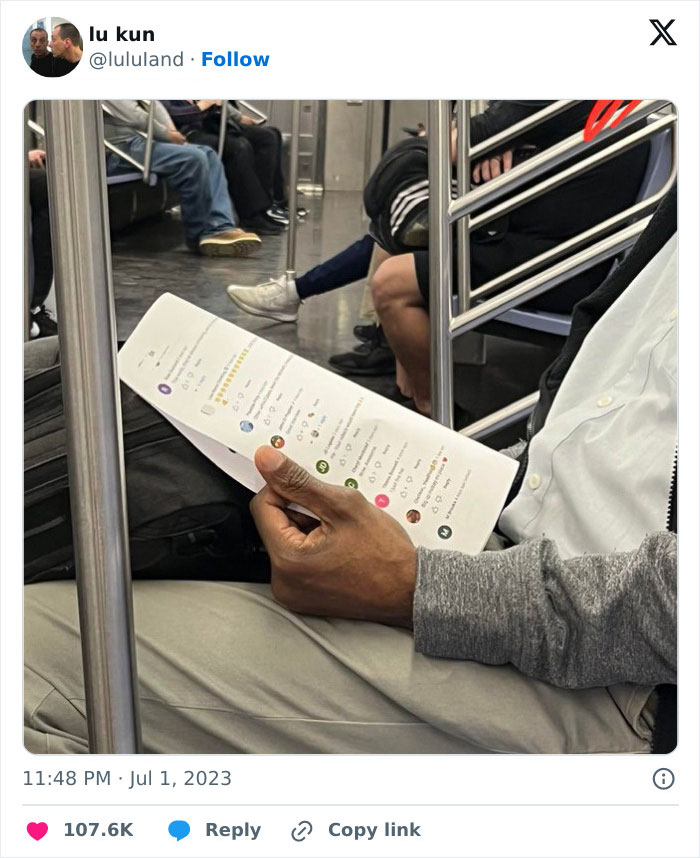 Subway passenger reading a printed boarding pass like a phone screen, holding it upright with one hand.