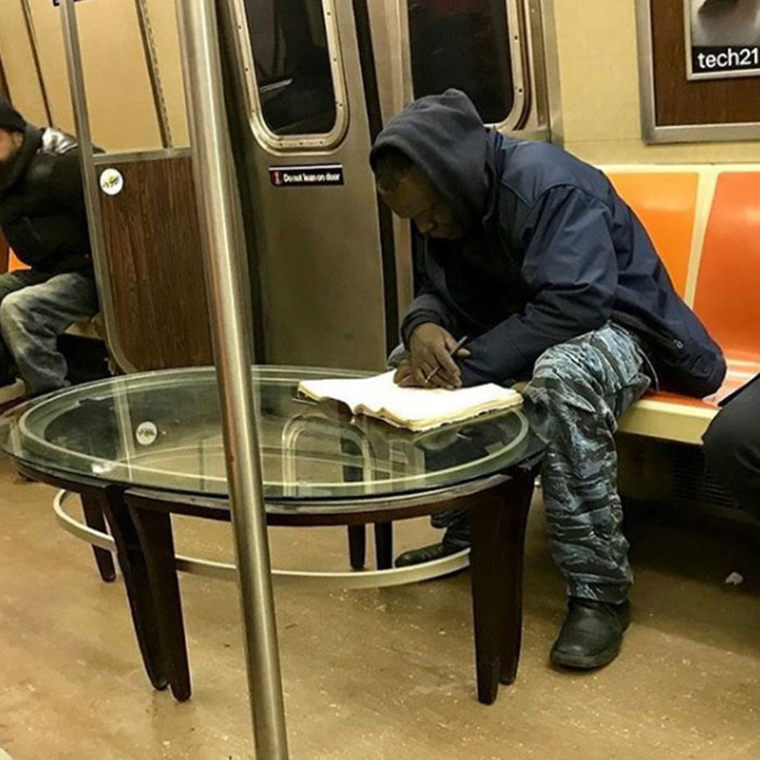 Passenger using a glass table as a desk on the subway, creating a funny train scene.