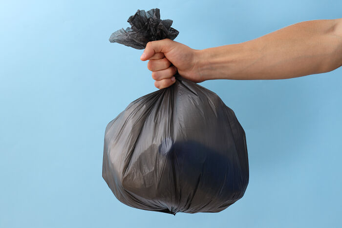 A hand holding a black garbage bag against a blue background, symbolizing expensive items worth reconsidering.