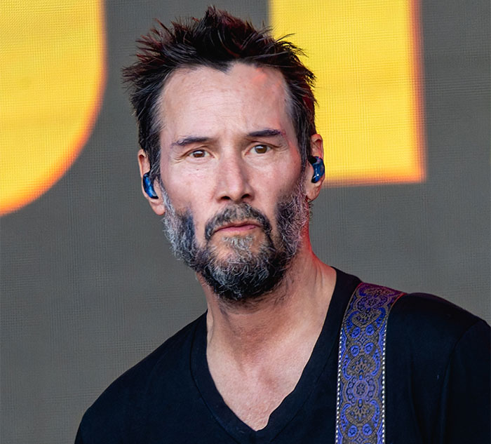 A celebrity with a beard wearing a black shirt and in-ear monitors, performing on stage.