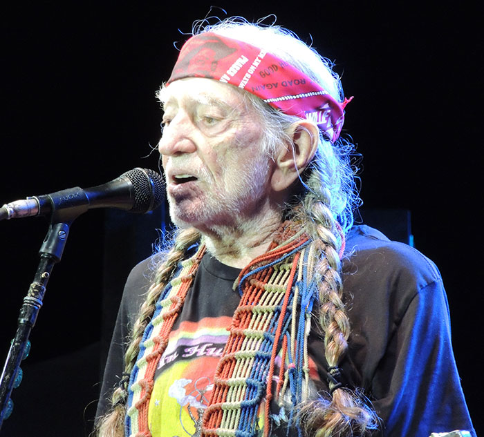 A celebrity wearing a bandana and braids, singing into a microphone on stage.