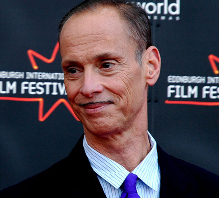 Celebrity at film festival, wearing a suit and purple tie.