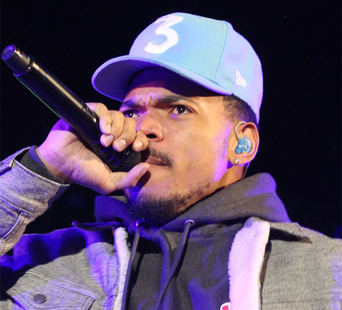 Celebrity performing on stage, wearing a blue cap and holding a microphone.