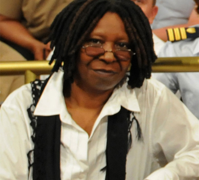 A person in glasses and a white shirt, sitting indoors, smiling at the camera.