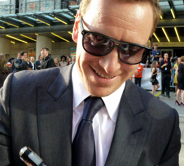 Celebrity in sunglasses and suit smiling at an event, interacting with fans.