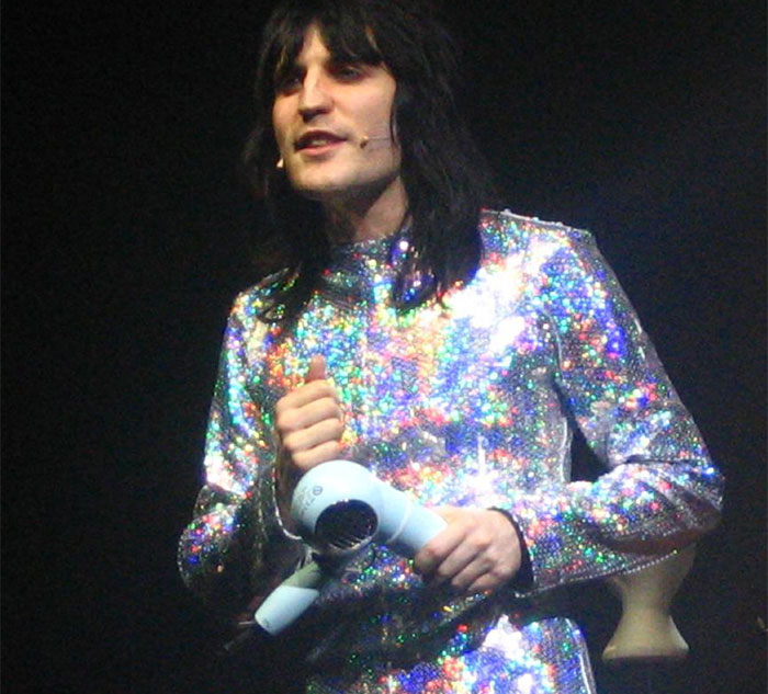 Celebrity in a glittery outfit holding a microphone on stage, exemplifying being nice in real life.