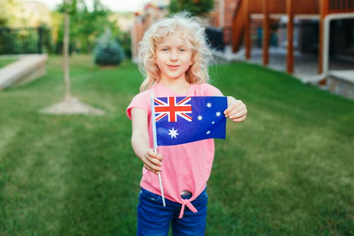 Child holding Australian flag in a garden, symbolizing kids feeling like foreigners in a different country.