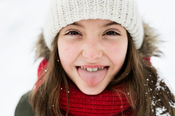 A young girl in winter clothing sticking her tongue out, representing carefree moments before adulthood for millennials.