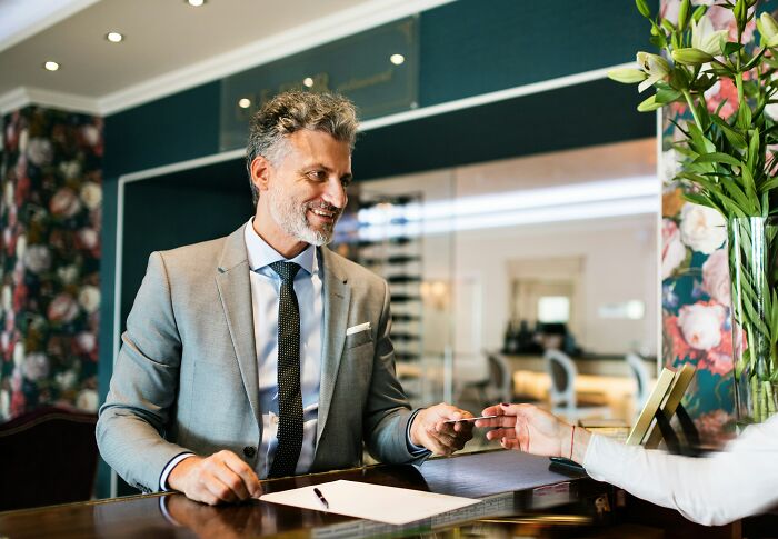 Man in a suit happily signing resignation at a hotel desk, illustrating a revengeful job exit.