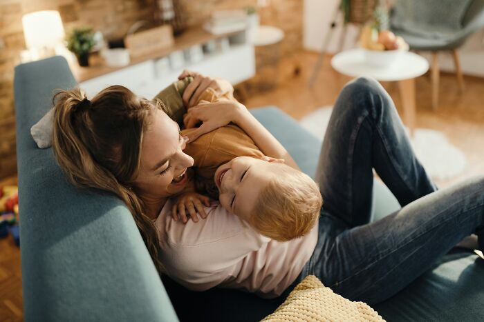 Mother and young child laughing together on a blue couch, illustrating family bonding in a foreign country.