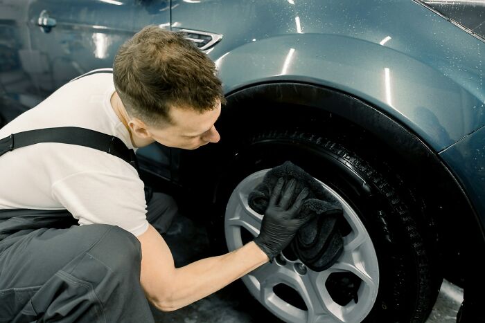 A man cleaning a car tire with a cloth, showcasing attention to detail.