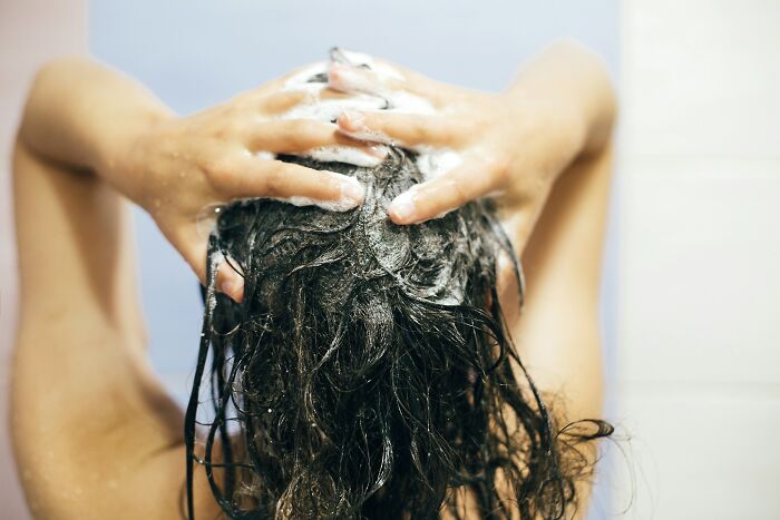 Person washing hair with luxurious shampoo, highlighting worth spending money on expensive items for hair care.