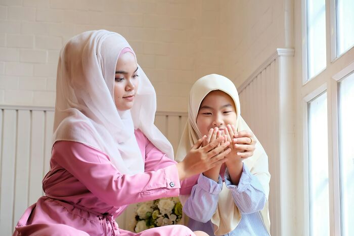 A woman and child in traditional attire share a moment by a window, illustrating kids feeling like foreigners in a different country.