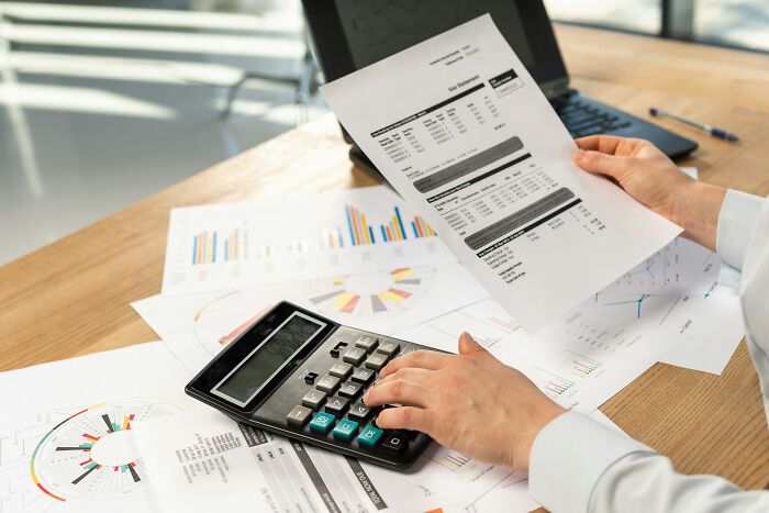 Hands holding financial papers and calculator on desk, examining data related to biggest scam human history.