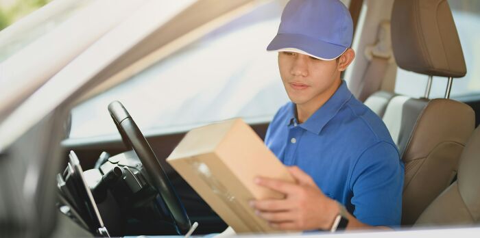 Delivery driver in blue uniform examines a package inside a car.