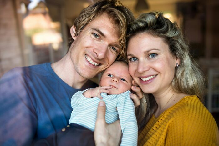 A smiling couple holding a baby in a cozy home setting, illustrating the feeling of being in a foreign country.