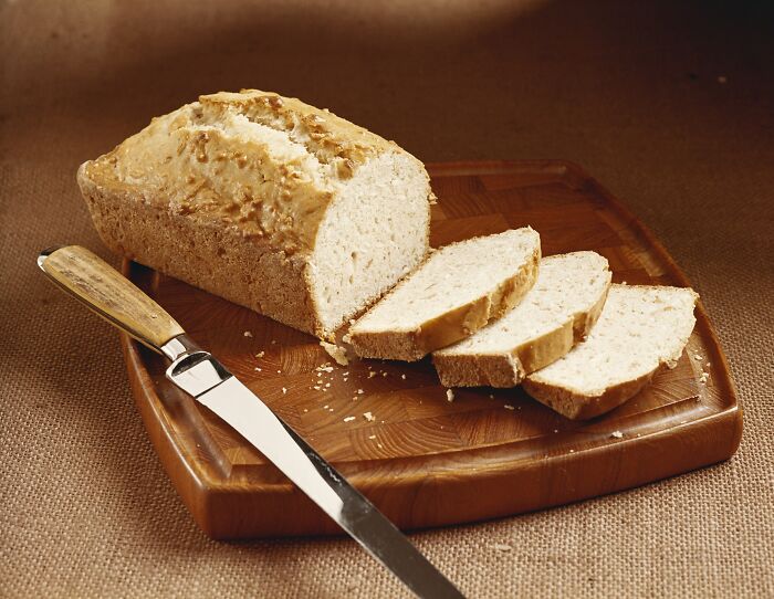 Sliced loaf of bread on a wooden board with a knife, symbolizing adulthood challenges for millennials.