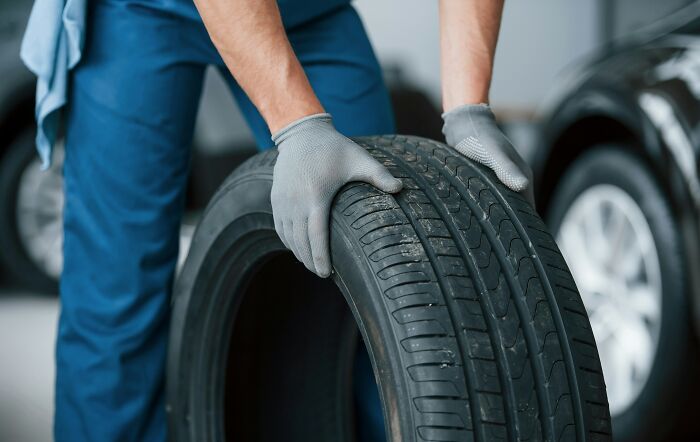 Person in gloves holding an expensive car tire, emphasizing items worth spending money on, near a vehicle.