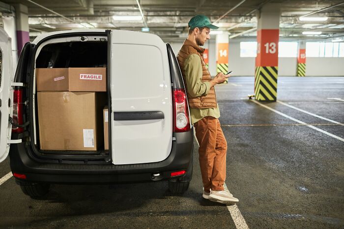 Person leaning on a van with boxes, likely reflecting on a savage job exit in a parking garage.