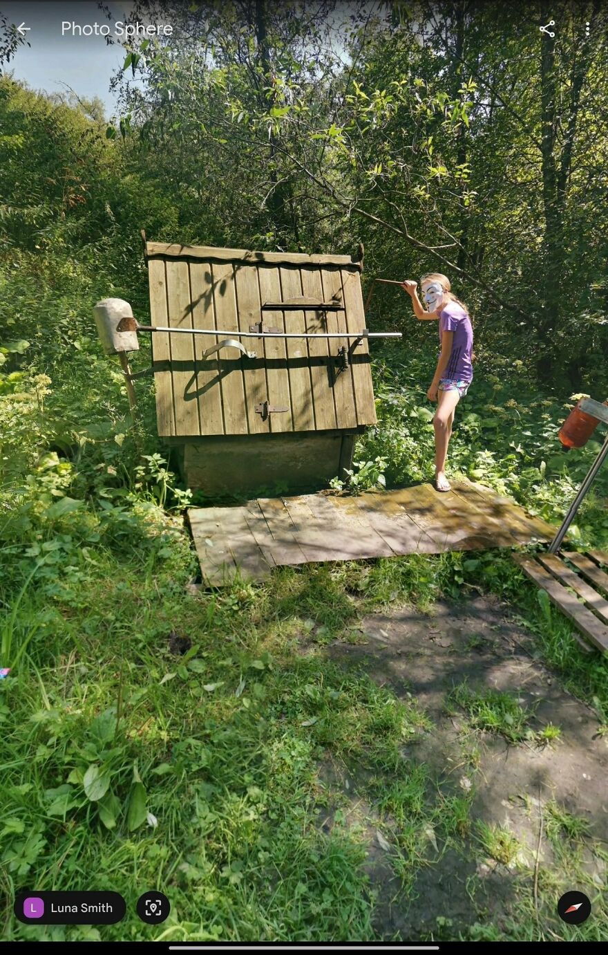 Child in mask by a wooden structure in a forest, captured on Google Earth.