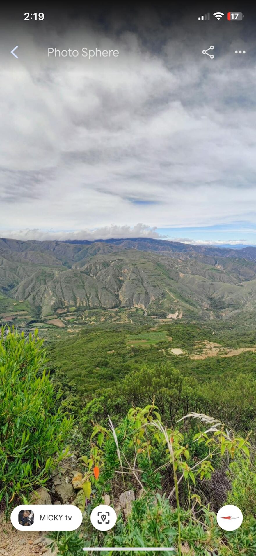 Strange mountain formations captured on Google Earth with greenery in the foreground under a cloudy sky.