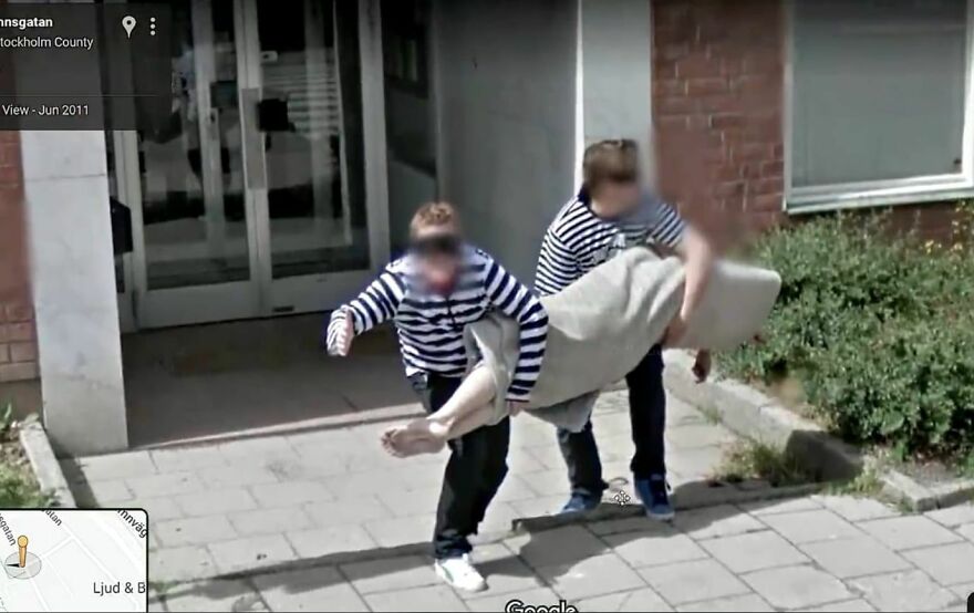 Two people in striped shirts carrying a large carpet on a sidewalk, captured on Google Earth.