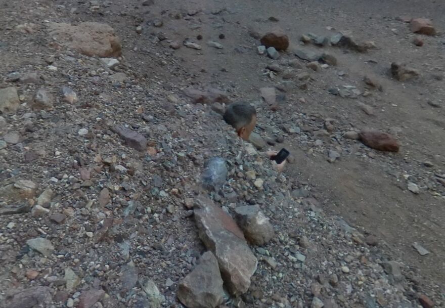 Strange find on Google Earth: a person embedded in rocky terrain, holding a phone, blending into surroundings.