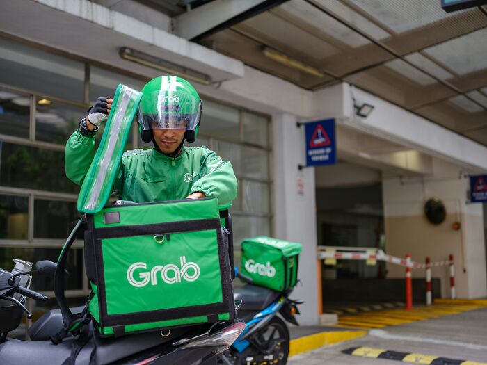 Delivery rider in green uniform with a Grab backpack, preparing for a delivery outside a building.