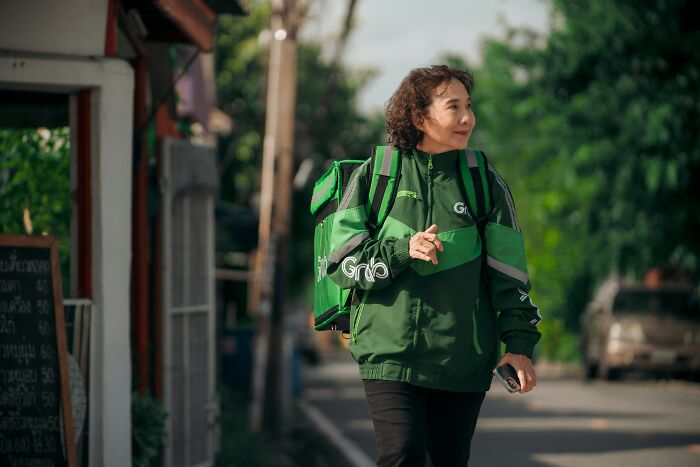 Delivery person in green uniform walking on street, carrying bags.