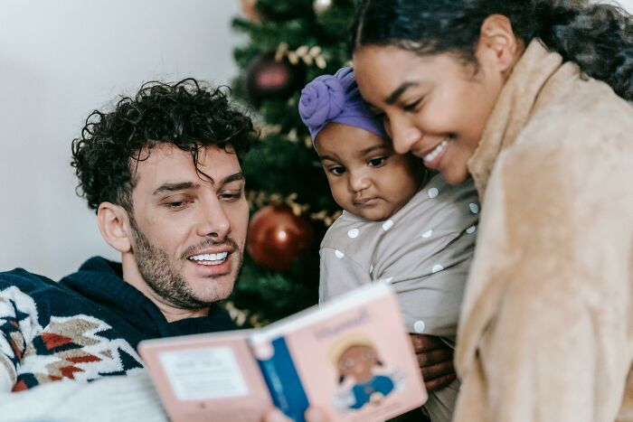 Family reading a book together, reflecting intentions about a babysitting offer and gift for parents from in-laws.