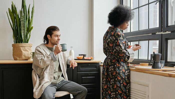 Couple in kitchen with coffee, discussing in-laws' babysitting offer and deadline implications.