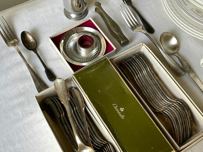 Silverware collection displayed on a white tablecloth, featuring boxed spoons, forks, and a Christofle brand box.