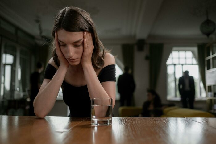 Woman in distress at a table with a glass of water, reflecting the silverware drama theme.